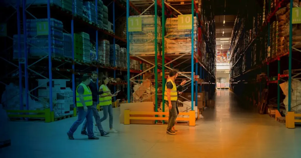 5 people walking past racks in a warehouse