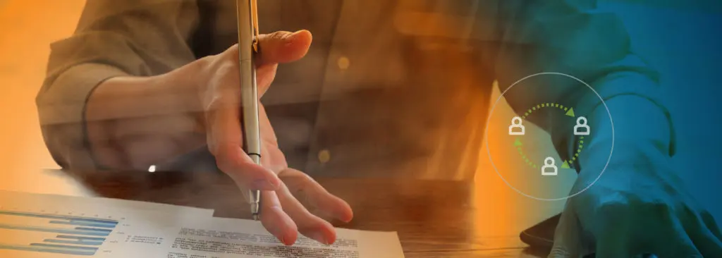 A hand with a pen with paperwork at desk