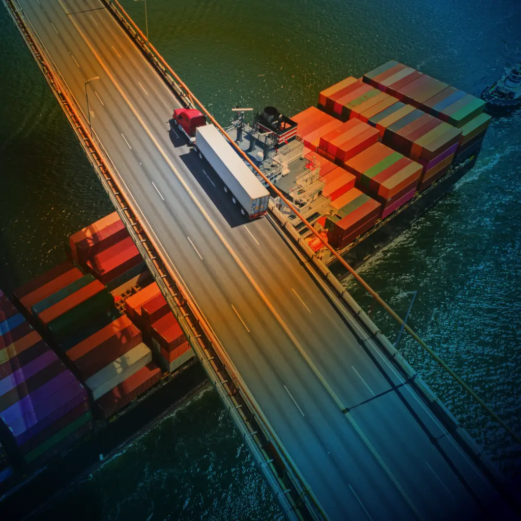 A truck going over a bridge with a container ship going under the bridge