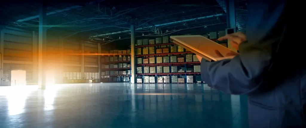 Persons tapping a tablet inside a warehouse with stock in the racking