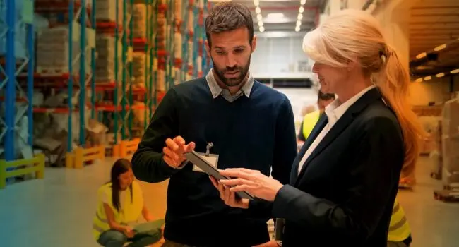Two people in a warehouse talking whilst pointing at a clipboard