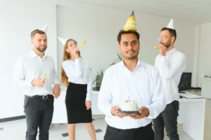 Image of people in office celebrating a birthday. The man at the front looks grumpy.