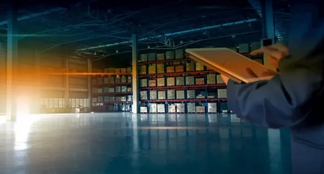 Persons tapping a tablet inside a warehouse with stock in the racking