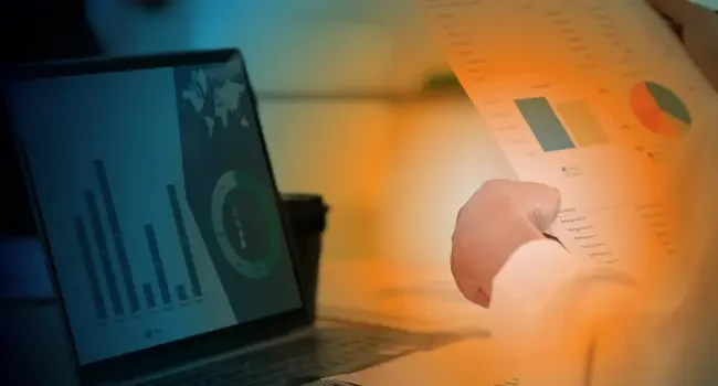 Hands holding a report in front of a laptop screen