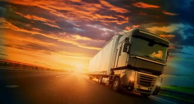 A truck driving towards camera with the sun setting behind it.