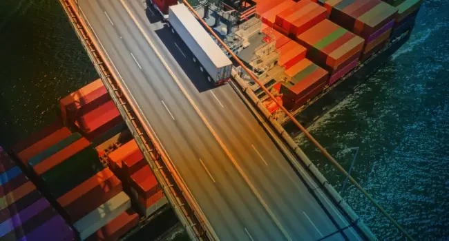 Aerial view of a truck crossing a bridge with a sea freight container going under the bridge
